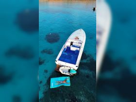 A person relaxes on a floating mat next to a stylish boat in crystal-clear waters, perfect for a day of sunbathing and leisure on the water.