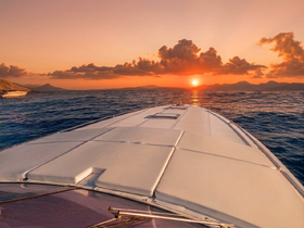 A stunning view from the front of a yacht as it cruises towards a vibrant sunset, showcasing the beauty of the open water and distant mountains.
