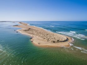 A stunning aerial view of a sandy island with boats anchored nearby, showcasing a picturesque beach and vibrant coastline — perfect for island hopping adventures.