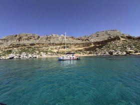 A picturesque sailboat anchored near a rocky coastline, surrounded by clear turquoise waters — an ideal setting for a relaxing day on the water.
