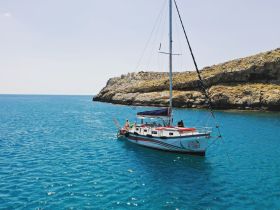 A beautiful sailboat named 'Gin & Tonic' anchored in crystal-clear waters, surrounded by stunning rocky cliffs — perfect for a serene day on the water.