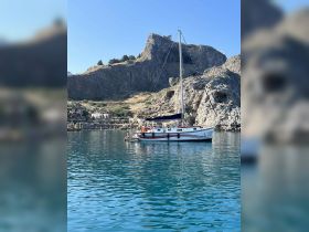 A picturesque scene featuring a boat anchored near a rocky coastline, with people enjoying the water — a perfect spot for swimming and relaxation.