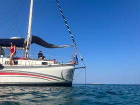 A lively group enjoys their time aboard a sailboat, with one person waving from the deck — a perfect snapshot of fun on the water.