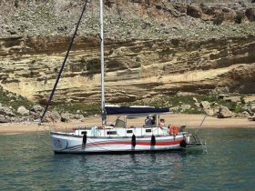 A sailboat anchored near a picturesque beach, with guests enjoying the serene surroundings — perfect for a day of relaxation and exploration on the water.