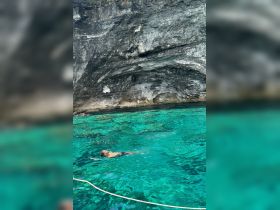 A swimmer enjoys the crystal-clear waters near a rocky cave, showcasing the stunning natural beauty of the area — perfect for adventure seekers and nature lovers.