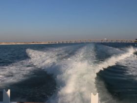 A stunning view of a boat underway, leaving a wake in the clear waters, with a bridge visible in the background — perfect for showcasing the beauty of boating adventures.