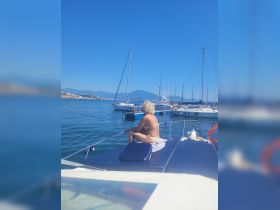 A woman enjoys a moment of relaxation on the deck of a boat, surrounded by stunning views of the marina and distant mountains — a perfect snapshot of a sailing adventure.
