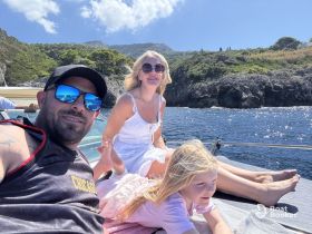 A joyful family enjoys a sunny day on the boat, capturing a perfect moment of relaxation and togetherness against a stunning coastal backdrop.