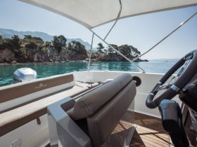 A well-appointed helm area inside a boat, showcasing comfortable seating and a clear view of the serene waters and rocky coastline — perfect for navigating coastal adventures.