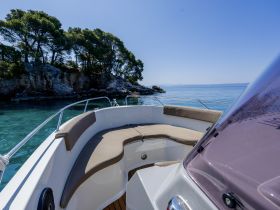 A serene view of the interior seating area of a boat, showcasing comfortable cushions and a beautiful backdrop of clear waters and lush greenery.