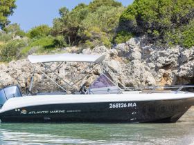 A sleek Atlantic Marine Open 670 speedboat docked in calm waters, showcasing its elegant design against a natural backdrop of rocks and greenery.