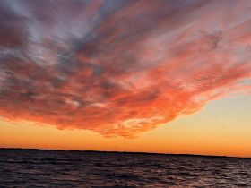 A stunning sunset over the water, featuring vibrant clouds and a serene atmosphere, perfect for capturing the beauty of nature.