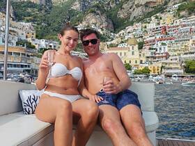 A couple enjoys cocktails on a boat with a stunning coastal backdrop, perfect for romantic getaways or celebrations along the Amalfi Coast.