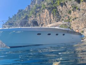 A stunning side view of a yacht anchored near a rocky coastline, showcasing its sleek design against the backdrop of lush greenery and clear waters.