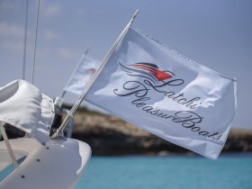 Close-up of the 'Latchi Pleasure Boats' flag on a yacht, showcasing the vessel's branding against a backdrop of clear turquoise waters.