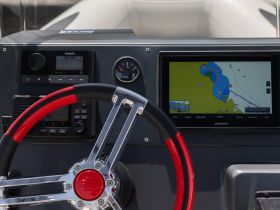Close-up view of a boat's helm featuring a modern steering wheel and navigation display, ideal for showcasing the vessel's control area.