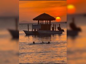 A picturesque sunset view featuring a tiki bar on the water, with swimmers enjoying the warm evening — a perfect scene for relaxation and fun in the Dominican Republic.