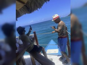 Two friends enjoy a sunny day by the ocean, capturing memories on their phones while relaxing on a boat — perfect for a fun day out on the water.