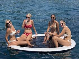 A group of friends enjoys a sunny day on the water, sipping cocktails while relaxing on a floating mat — the perfect setting for summer fun and celebrations.