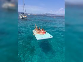 A lively group enjoys a sunny day on a floating mat in crystal-clear waters, perfect for summer fun and relaxation.