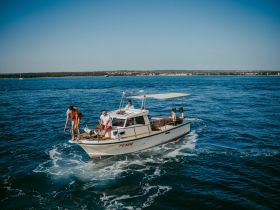 A lively group enjoys a day on the water, with one person preparing to jump off the boat while others relax — perfect for summer adventures and fun on the sea.