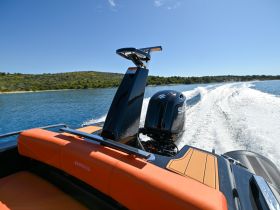 A sleek speedboat in motion, showcasing its powerful engine and stylish design against a backdrop of serene waters and lush greenery.