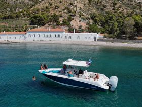 A lively group enjoys a day on the water, with some swimming near their boat against a picturesque coastal backdrop. Perfect for summer adventures and fun outings.