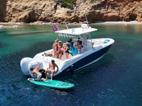 A lively group enjoys a fun day on the water, with paddleboarding and celebrations aboard their boat, 'Mojito,' surrounded by stunning coastal scenery.