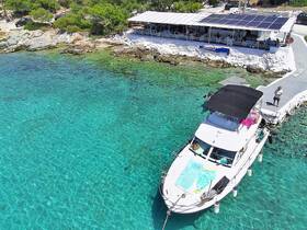 Aerial view of a boat docked in crystal-clear waters, with a scenic backdrop of a waterfront restaurant and lush greenery — perfect for a relaxing day on the water.