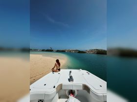 A woman relaxes on the bow of a boat, enjoying the serene view of a secluded beach and turquoise waters — a perfect escape for sunbathing and tranquility.