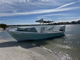 A fishing boat rests on the shore, showcasing its sleek design against a backdrop of clear skies and calm waters — perfect for a day of fishing or leisure on the water.
