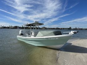 A sleek speedboat docked on a sandy shore, showcasing its design against a backdrop of clear blue skies and calm waters — perfect for fishing or leisure outings.
