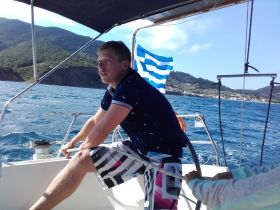 A young man actively sailing on a boat, with scenic mountains in the background — a perfect moment capturing the thrill of sailing adventures.