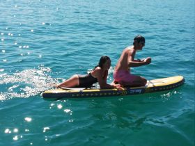 A couple enjoys paddleboarding together in clear turquoise waters, showcasing a fun and adventurous day on the water.