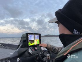 A young angler navigates a fishing boat while using sonar technology to locate fish, showcasing the excitement of a fishing adventure on the water.