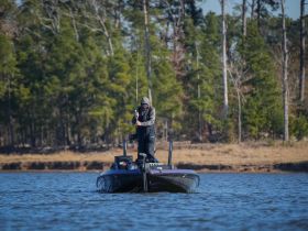 A fisherman casts his line from a sleek boat, enjoying a peaceful day on the water surrounded by nature — perfect for fishing enthusiasts.