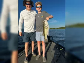 A father and son proudly display their catch of the day, a large bass, while enjoying a fishing trip on the water — a perfect bonding experience in the great outdoors.