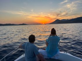 A couple enjoys a stunning sunset while aboard a boat, capturing the moment with their cameras — a perfect romantic getaway on the water.