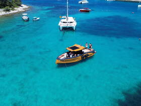 A lively group enjoys a day on a stylish boat in crystal-clear turquoise waters, perfect for swimming and relaxation.
