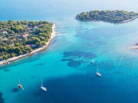 A stunning aerial view of sailboats anchored near a picturesque island, showcasing the vibrant turquoise waters and lush greenery — an ideal destination for sailing enthusiasts and nature lovers.