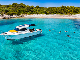 A lively group enjoys swimming in the crystal-clear turquoise waters near a boat, showcasing the perfect summer day on the water.
