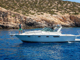 A man stands confidently at the bow of a boat, surrounded by stunning blue waters and a rocky coastline, capturing the essence of adventure on the open sea.