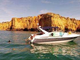 A group enjoys a sunny day on the water, with one person swimming near the boat and stunning cliffs in the background, perfect for a coastal adventure.