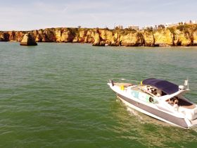 A sleek boat navigates the stunning coastline, showcasing vibrant cliffs and clear waters — an ideal scene for a memorable day on the water.