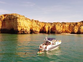 A lively group enjoys a day on the water near stunning coastal cliffs, with some swimming and others relaxing on the boat — a perfect summer getaway.