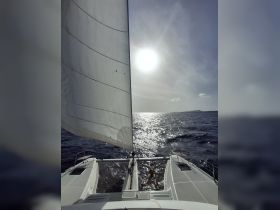 A person relaxes on the netting of a catamaran while sailing under the sun, capturing the essence of a perfect day on the water.