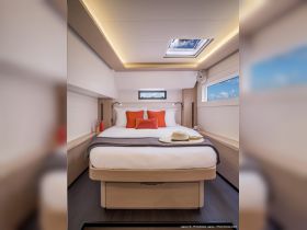 A beautifully designed cabin interior of a Lagoon 46, featuring a cozy bed with vibrant cushions and ample natural light, perfect for relaxing during a sailing adventure.