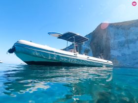 A striking view of a sleek boat gliding through crystal-clear waters, set against a stunning cliff backdrop — perfect for exploring coastal destinations.
