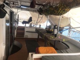 A cozy interior view of a boat's cabin featuring seating, a helm, and a table adorned with fresh fruits, ideal for relaxing and enjoying the journey.