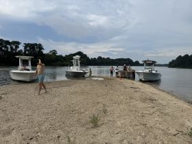 A lively group enjoys a day at the beach with two boats anchored nearby, perfect for swimming and fun in the sun.